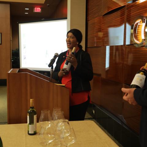 Maki Mandela speaks at a podium holding a wine bottle from her House of Mandela collection